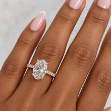 Load image into Gallery viewer, An oval diamond ring with a rose gold band, featured on a hand with a light gray background.