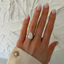 Load image into Gallery viewer, A close-up of a hand wearing a silver ring with a pear-cut clear gemstone, set against a textured white fabric background.