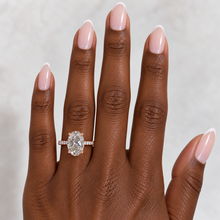 Load image into Gallery viewer, An oval diamond ring with a rose gold band, featured on a hand with a light gray background.

