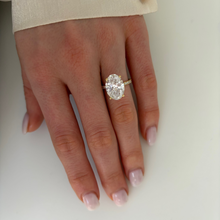 Load image into Gallery viewer, A close-up of a hand wearing a yellow gold ring with a large oval-cut clear gemstone and smaller accent stones, shown against a plain light background.
