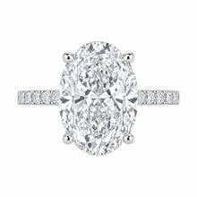 Load image into Gallery viewer, An oval diamond engagement ring with a brilliant-cut center stone in a four-prong setting, flanked by a pavé-set diamond band in a silver-colored metal, shown on a plain white background.
