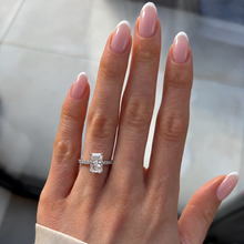 Load image into Gallery viewer, A close-up of a hand with manicured nails wearing a silver engagement ring with a rectangular clear gemstone. The hand is resting on a light gray surface.
