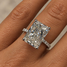 Load image into Gallery viewer, A close-up of a ring worn on a finger, featuring a large rectangular clear gemstone in a silver-toned setting with small side stones.
