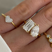 Load image into Gallery viewer, A close-up of a hand wearing multiple yellow gold rings, including a Emerald cut and Pear cut Toi Et Moi ring, a heart-shaped ring with pavé stones,, and other gold rings with small round stones.
